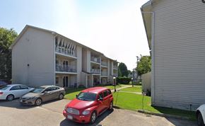 Gananoque apartment for rent - A red car is parked in front of a white building with a balcony.
