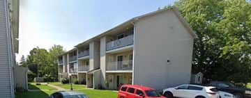 Gananoque apartment for rent - A red car is parked in front of a white building with a balcony.