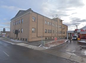 Cornwall apartment for rent - A large brick building with a flat roof and a parking lot in front.