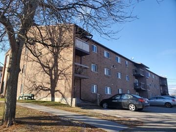 Smiths Falls apartment for rent - A black car is parked on the side of a road in front of a brick building.