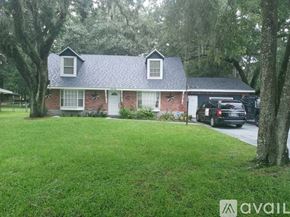 Brooksville apartment for rent - A house with a brick facade and a white door is surrounded by a grassy lawn and trees.