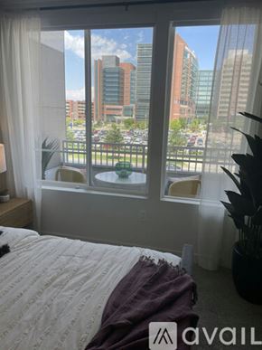 Aurora apartment for rent - A bedroom with a large window overlooking a parking lot and buildings.