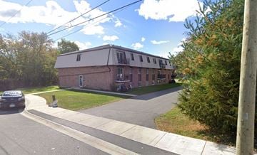 Napanee apartment for rent - A brick building with a white roof is surrounded by trees and grass.