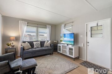 Zephyrhills house for rent - A living room with a grey couch, a chair, a table with a lamp and a plant, a television on a stand, and a rug on the floor.