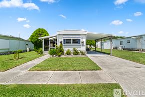 Zephyrhills house for rent - A house with a white exterior and a grey roof is surrounded by a well-maintained lawn and a clear blue sky.