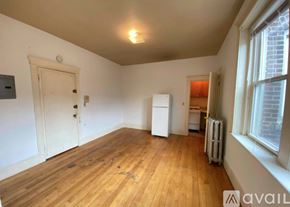 Boston apartment for rent - A room with wooden floors and white walls, with a door, a window, and a radiator.