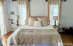 San Diego house for rent - A bed with a beige comforter and pillows is in the center of a room with two lamps on side tables.