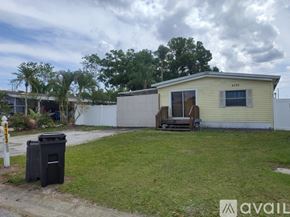 Clearwater apartment for rent - A small house with a yellow exterior is surrounded by a grassy area and a trash can is placed on the left side of the image.