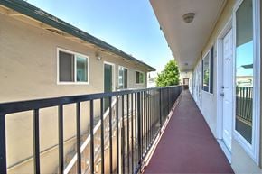 Redwood City apartment for rent - a balcony with a red walkway next to a building with white doors