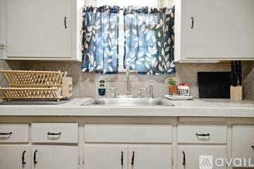 Lubbock townhouse for rent - A kitchen with white cabinets and a window with a blue and white curtain.