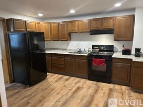 Bellefonte apartment for rent - A black refrigerator stands in a kitchen with wooden cabinets and a black stove.