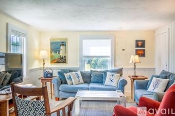 Sandwich house for rent - A living room with a blue couch and a painting of a lighthouse on the wall.