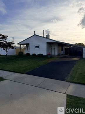 Levittown house for rent - A small white house with a brown fence and a tree in front.