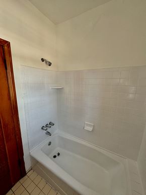Los Angeles apartment for rent - A white tiled bathroom with a white bathtub and a wooden door.