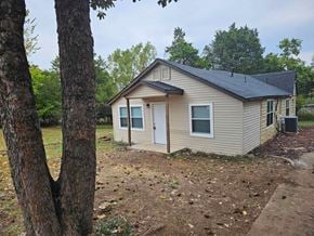 Choctaw house for rent - A small house with a brown roof and a white door is surrounded by trees.