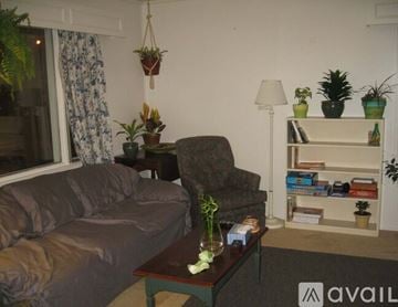 Syracuse house for rent - A living room with a grey couch, a table with a vase of flowers, and a bookshelf with various items.