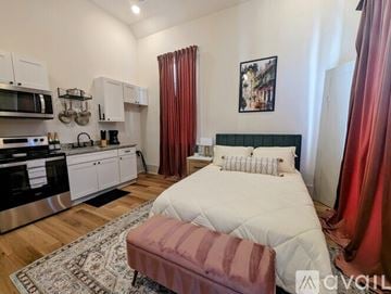 New Orleans apartment for rent - A bedroom with a bed, a bench, and a kitchen area with a microwave and oven.