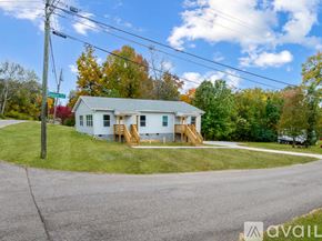 Knoxville townhouse for rent - A house with a white exterior and a grey roof is surrounded by green grass and trees.