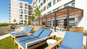 Oak Park apartment for rent - Outdoor sundeck at Eleven33 Apartments in Oak Park featuring blue lounge chairs, greenery, and grilling stations under a modern pergola.