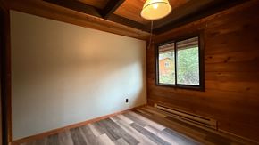 Sitka house for rent - A room with wooden walls and a window showing a view of a house and trees.