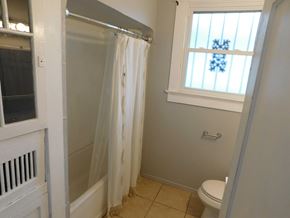 New Orleans apartment for rent - A bathroom with a toilet, a shower with a curtain, and a window.
