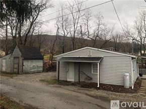Lemont Furnace house for rent - A house with a grey siding and a white door is situated in a rural area.