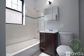 Chicago apartment for rent - A modern bathroom with a white tub, a white toilet, a sink, and a window.