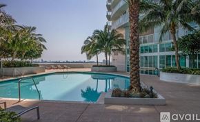 Miami condo for rent - A pool surrounded by palm trees and a building in the background.