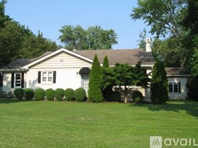 St. Louis house for rent - A white house with a brown roof and a chimney is surrounded by green trees and bushes.