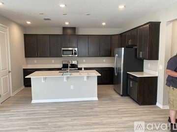 Haines City house for rent - A man is standing in a kitchen with a refrigerator, microwave, and oven.