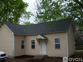 Eau Claire house for rent - A small house with a white door and windows is surrounded by trees.