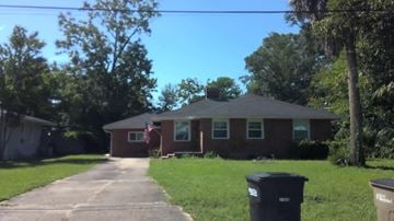 Pensacola house for rent - A house with a flag on the front and a trash can in front of it.