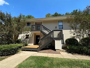 Winston Salem apartment for rent - A house with a beige siding and a black door is surrounded by green bushes.