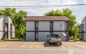 Bryan apartment for rent - A silver pickup truck is parked in a parking lot in front of a two-story building with a brown roof.