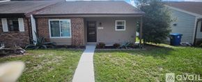 Dade City house for rent - A small house with a brown brick exterior and a grey siding is shown with a white walkway leading to the front door.