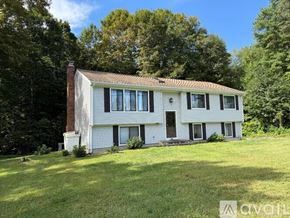 Simsbury house for rent - A white house with a brown roof is surrounded by green trees.