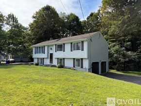 Simsbury house for rent - A two-story house with a white exterior and a grey roof is surrounded by a grassy yard and trees.