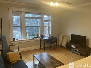 Boston apartment for rent - A living room with a blue couch, a coffee table, a television, and a window with a view of a city.