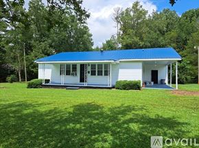 Warrenton apartment for rent - A white house with a blue roof is surrounded by greenery.