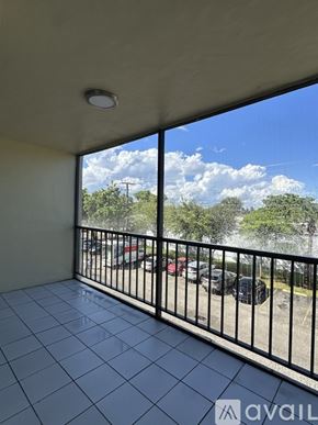 Miami apartment for rent - A balcony with a black railing and a view of a parking lot and trees.