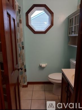 Stafford house for rent - A bathroom with a toilet, a hexagonal mirror, and a tiled wall.