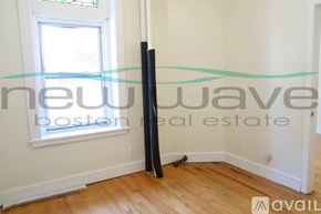 Boston apartment for rent - A room with a wooden floor and a window, with a large black object leaning against the wall.