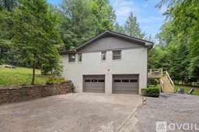 Asheville house for rent - A house with a stone wall and two garages is surrounded by trees.
