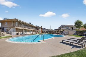 Fullerton apartment for rent - A large outdoor swimming pool surrounded by a grassy area and a building in the background.