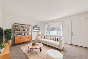 Fullerton apartment for rent - A living room with a white couch, a wooden coffee table, and a large window with blinds.