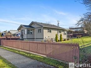 Seattle apartment for rent - A house with a grey roof and a white fence is surrounded by a green lawn.
