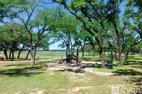 Lago Vista house for rent - A playground with a swing set surrounded by trees.