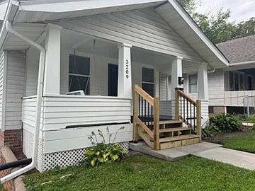 Omaha apartment for rent - A white house with a porch and a wooden railing.