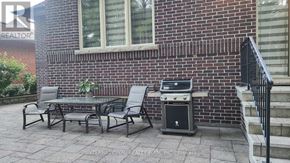 Toronto (Stonegate-Queensway) house for rent - A patio with a grill and chairs is in front of a brick building.