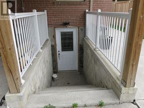 Toronto (Downsview-Roding-Cfb) house for rent - A white door with a glass window is in the middle of a concrete area with a wooden railing on either side.